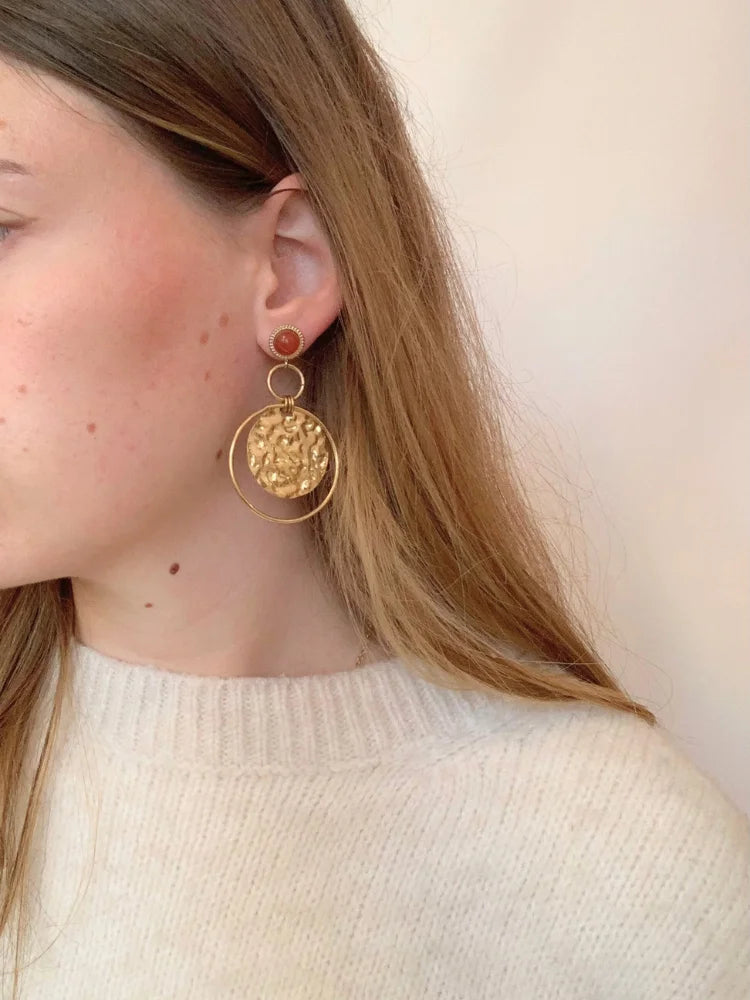 La femme porte les boucles d'oreilles Lucie dorées en acier inoxydable de chez Au Bonheur de Sophie